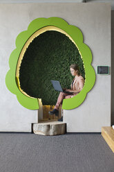 Designer working on laptop in tree shaped office space - CUF25328