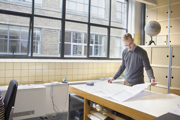 Male designer looking at blueprint in creative office - CUF25346