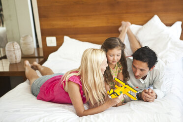 Young family lying on bed, playing with toy plane - CUF25383