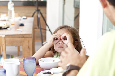 Father and daughter sitting at breakfast table, daughter making binoculars from fingers - CUF25386