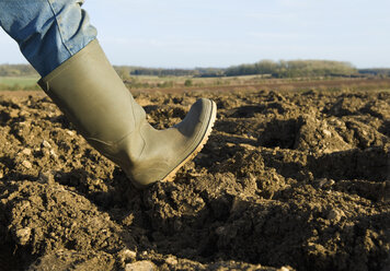 Close up of farmers rubber boot walking on ploughed field - CUF25462