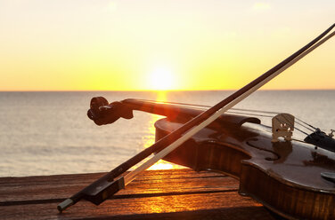 Sonnenuntergang über dem Meer mit Geige und Bogen auf einer Bank - CUF25589