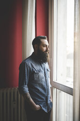 Young bearded man standing by window - CUF25612