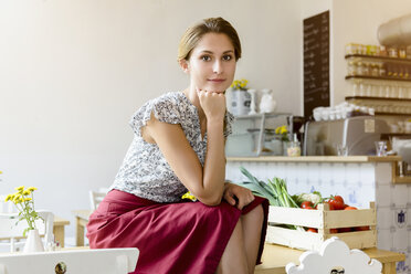 Young woman sitting on cafe table looking at camera, portrait - CUF25647