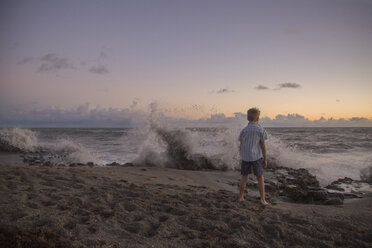 Rückansicht eines Jungen, der bei Sonnenaufgang die plätschernden Wellen beobachtet, Blowing Rocks Preserve, Jupiter Island, Florida, USA - ISF09424