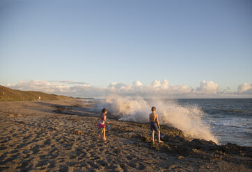 Boy and sister watching splashing waves from beach, Blowing Rocks Preserve, Jupiter Island, Florida, USA - ISF09428