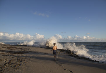 Rückansicht eines Jungen, der den Strand mit plätschernden Wellen erkundet, Blowing Rocks Preserve, Jupiter Island, Florida, USA - ISF09435