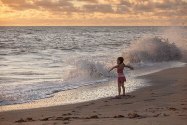 Mädchen mit offenen Armen, während die Wellen bei Sonnenaufgang plätschern, Blowing Rocks Preserve, Jupiter Island, Florida, USA - ISF09437