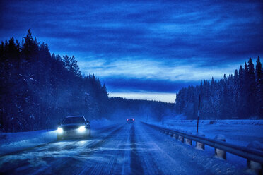 Autoscheinwerfer auf schneebedeckter Landstraße in der Dämmerung, Hemavan, Schweden - CUF25785