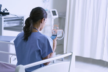 Sanitäterin sitzt auf einem Krankenhausbett und liest Smartphone-Texte - CUF25800