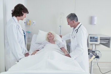 Two doctors talking to senior female patient in hospital bed - CUF25806