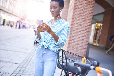 Portrait of smiling woman with earphones and cell phone in the city - ABIF00556