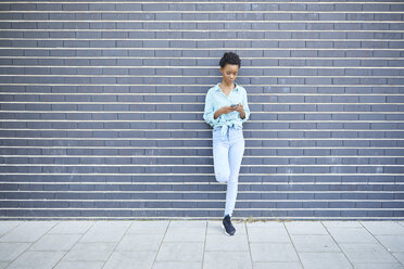 Woman standing in front of grey facade using cell phone - ABIF00571