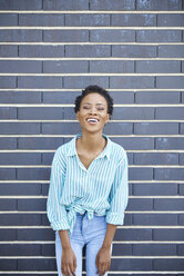 Portrait of laughing woman standing in front of grey facade - ABIF00572