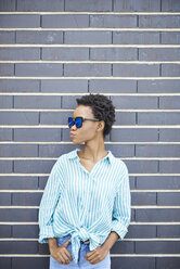 Woman with sunglasses standing in front of grey facade waiting - ABIF00574