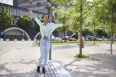 Happy young woman balancing on bench - ABIF00580