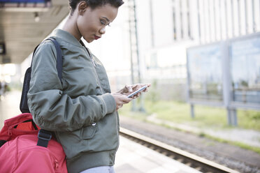 Junge Frau steht auf dem Bahnsteig und schaut auf ihr Handy - ABIF00590