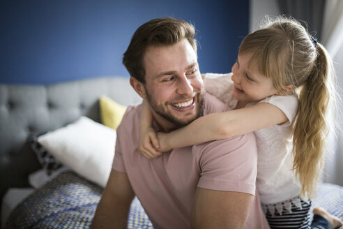 Glücklicher Vater und Tochter auf dem Bett sitzend, sich umarmend - AWF00007
