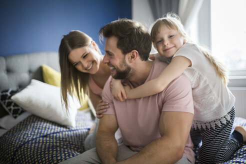 Glückliche Familie auf dem Bett sitzend, sich umarmend - AWF00009