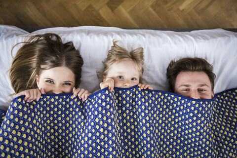 Glückliche Familie im Bett liegend, unter einer Decke versteckt, lizenzfreies Stockfoto