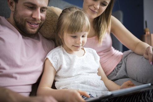 glückliche Familie, die auf dem Bett sitzt und mit ihrer kleinen Tochter etwas auf einem digitalen Tablet anschaut - AWF00024