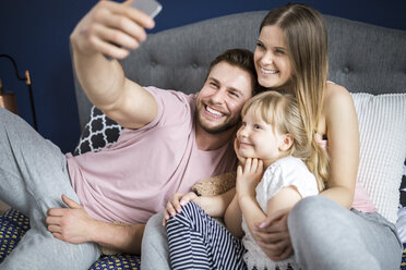 Glückliche Familie auf dem Bett sitzend, Smartphone-Selfies machend - AWF00026