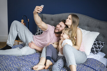 Happy family sitting on bed, taking smartphone selfies - AWF00027