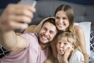 Happy family sitting on bed, taking smartphone selfies - AWF00028