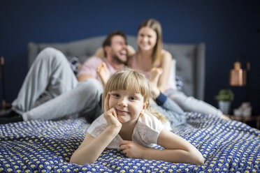 Cheeky little girl lying on bed with her parents - AWF00029