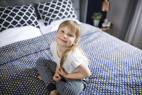 Blondes kleines Mädchen sitzt auf dem Bett und lächelt - AWF00036