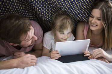 Eltern, die mit ihrer Tochter unter der Bettdecke etwas auf einem digitalen Tablet ansehen - AWF00038