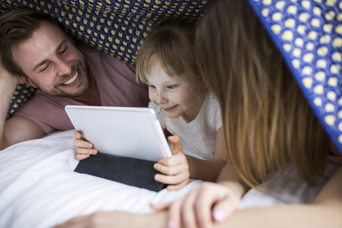 Eltern, die mit ihrer Tochter unter der Bettdecke etwas auf einem digitalen Tablet ansehen - AWF00039