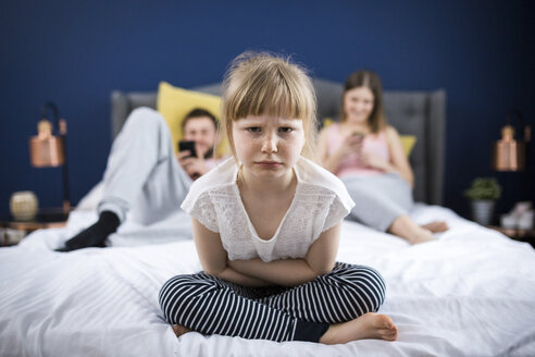 Wütendes kleines Mädchen auf dem Bett sitzend mit ihren Eltern - AWF00040