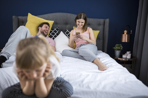 Vernachlässigtes kleines Mädchen, das mit seinen Eltern auf dem Bett sitzt und Smartphones benutzt - AWF00041