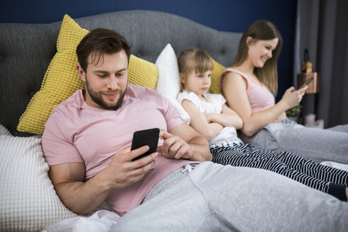 Neglected little girl sitting on bed with her parents, using smartphones - AWF00043