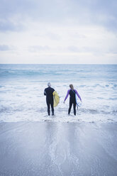 Father and daughter with surfboards walking into sea - CUF25967