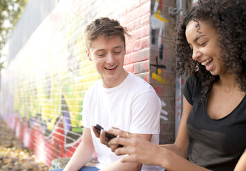 Teenager-Pärchen mit Smartphone gegen Wand mit Graffiti - CUF25985