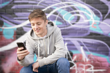 Teenager mit Smartphone gegen Wand mit Graffiti - CUF25990
