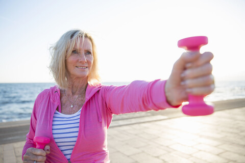 Ältere Frau beim Training mit Gewichten am Strand, lizenzfreies Stockfoto