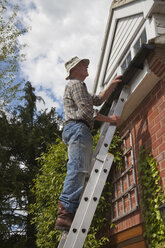 Senior man on ladder fixing gutter - CUF26072