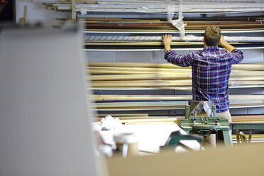 Rear view of man searching stockroom shelves in picture framers workshop - CUF26130