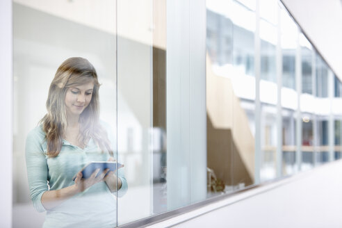 Geschäftsfrau mit digitalem Tablet hinter Bürofenster - CUF26138