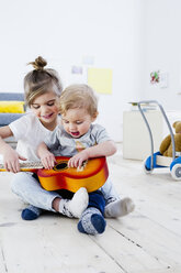 Bruder und Schwester spielen Spielzeuggitarre zu Hause - CUF26199