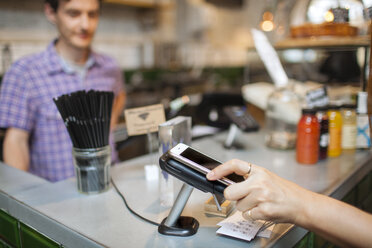 Ausgeschnittene Aufnahme einer Kundin, die in einem Café mit ihrem Smartphone kontaktlos bezahlt - CUF26345