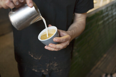 Männlicher Barista gießt mit den Händen Milch in eine Kaffeetasse in einem Café - CUF26359