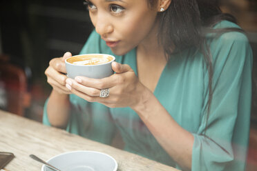 Mittlere erwachsene Frau hält Kaffeetasse und schaut aus dem Fenster eines Cafés - CUF26360