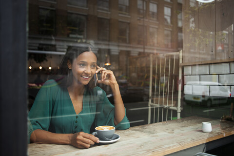 Mittlere erwachsene Frau, die auf dem Fensterplatz eines Cafés mit ihrem Smartphone chattet, lizenzfreies Stockfoto