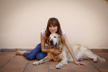 Portrait of mid adult woman petting dog on kitchen floor - CUF26483