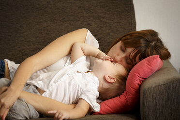 Mid adult woman reclining and kissing toddler daughter on sitting room sofa - CUF26488