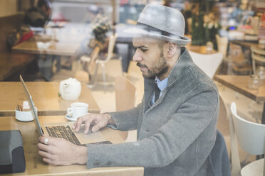 Geschäftsmann sitzt vor dem Fenster eines Cafés und benutzt einen Laptop - CUF26582